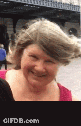 Woman In Pink Shirt Smiling With Windblown Hair GIF