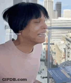 Woman In Pink Shirt Standing On Balcony Eyes Closed GIF