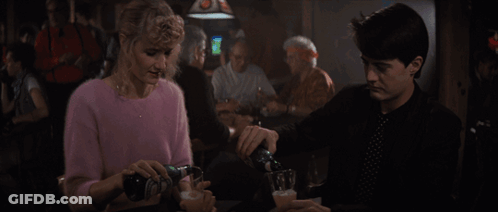 Woman In Pink Sweater Holding Beer Next To Man In Black Shirt GIF
