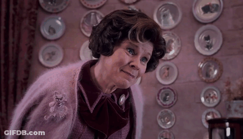 Woman In Pink Sweater In Front Of Wall With Plates GIF