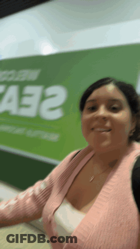 Woman In Pink Sweater Smiling In Front Of A33 Sign GIF