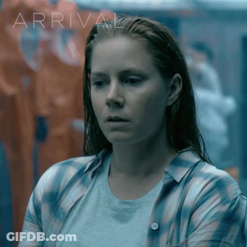Woman In Plaid Shirt In Front Of Arrival Sign GIF