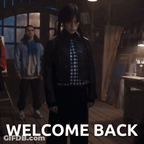 Woman In Plaid Shirt In Front Of Welcome Back Sign GIF