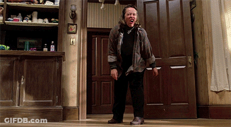 Woman In Plaid Shirt Standing In Front Of Door With Mouth Open GIF