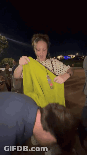 Woman In Polka Dot Shirt Holding Yellow Shirt Over Man's Head GIF