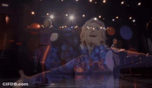 Woman In Purple And Orange Jacket Singing Into Microphone GIF