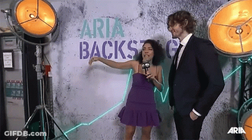 Woman In Purple Dress Talking To Man In Suit Backstage GIF