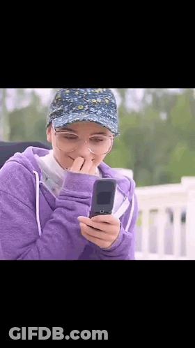 Woman In Purple Hoodie And Hat Looking At Phone GIF