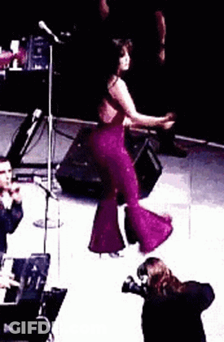 Woman In Purple Jumpsuit Dancing On Stage While Man Takes Photo GIF