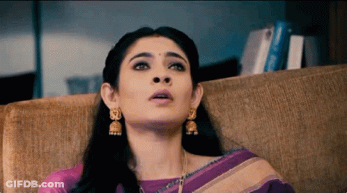 Woman In Purple Saree And Gold Earrings Sitting On Couch GIF