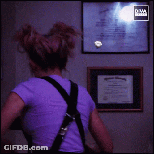 Woman In Purple Shirt And Black Overalls Smiling In Front Of Diva Screen GIF