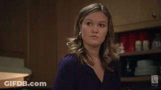 Woman In Purple Shirt And Earrings Standing In Kitchen GIF