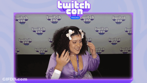 Woman In Purple Shirt Smiling In Front Of Twitch Con Wall GIF