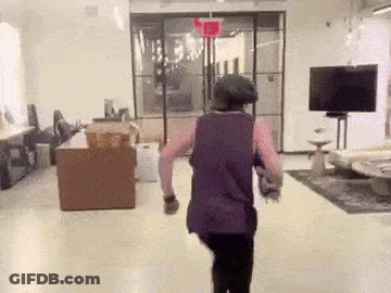 Woman In Purple Tank Top Walking Under Red Exit Sign GIF