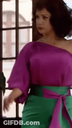 Woman In Purple Top And Green Pants Standing By Window GIF