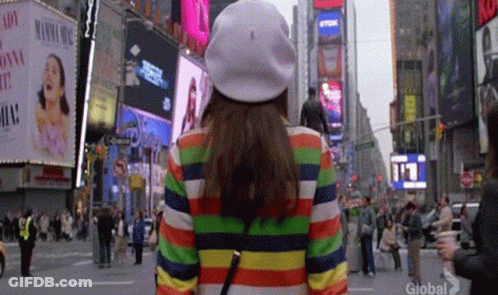 Woman In Rainbow Striped Jacket And White Hat Walking GIF