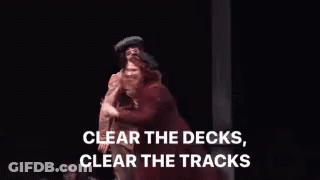 Woman In Red Coat On Stage Before Man In Brown Jacket GIF