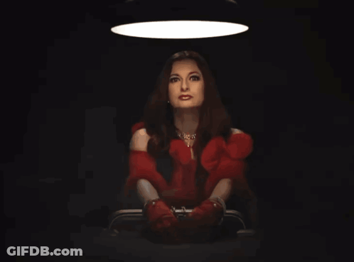 Woman In Red Dress And Red Gloves Sitting In Dark Room GIF