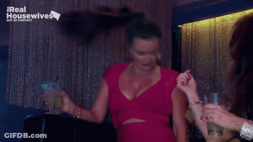 Woman In Red Dress Holding Drink In Front Of Real Housewives Sign GIF