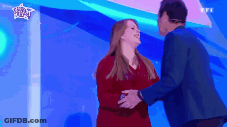 Woman In Red Dress Hugging Man In Blue Suit In Front Of Coup D'Envo Sign GIF