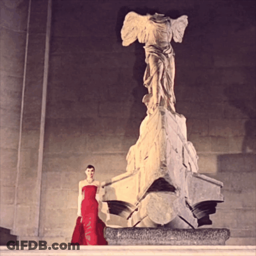 Woman In Red Dress Next To Statue GIF