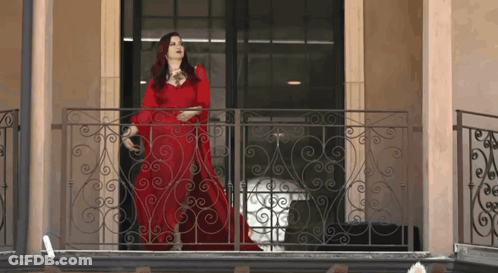 Woman In Red Dress On Balcony With Wrought Iron Railing GIF