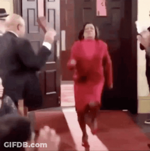 Woman In Red Dress Running On Red Carpet, Man In Suit Behind GIF