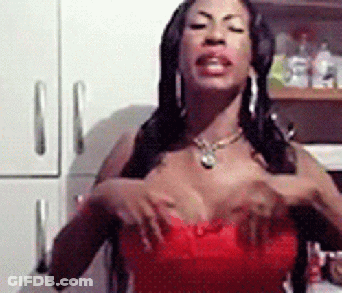 Woman In Red Dress Standing In Kitchen With Hands On Breasts GIF