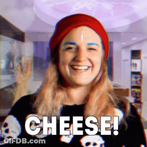 Woman In Red Hat And Skull Shirt Saying Cheese GIF