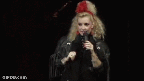 Woman In Red Headband And Black Jacket Singing Into Microphone GIF