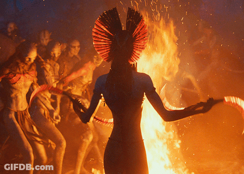 Woman In Red Headdress Standing In Front Of Fire GIF