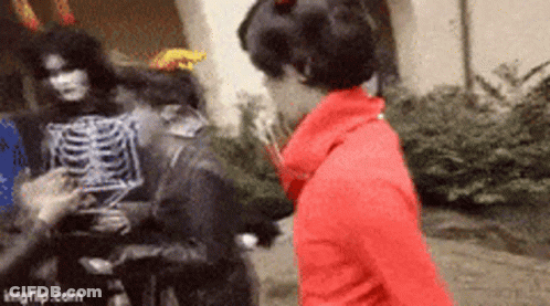 Woman In Red Jacket Next To Skeleton Costume GIF