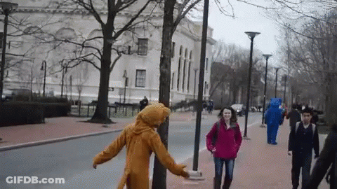 Woman In Red Jacket Walking With Man In Bear Costume Behind GIF