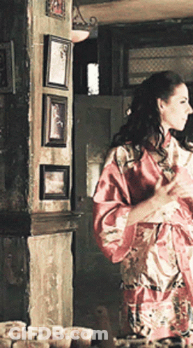 Woman In Red Robe Standing Before Wall Of Pictures GIF