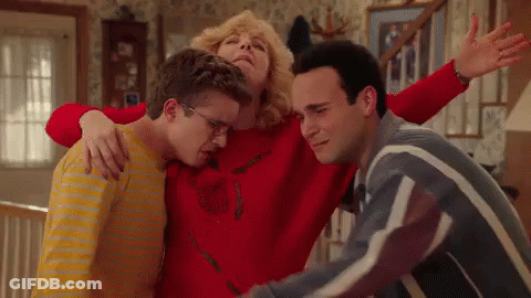 Woman In Red Sweater Hugging Two Young Men GIF