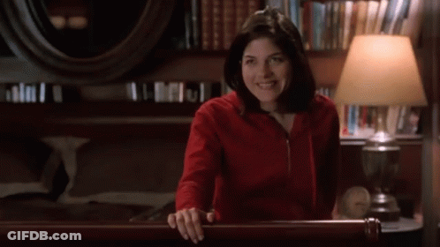 Woman In Red Sweatshirt Smiling In Room With Lamp GIF