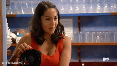 Woman In Red Tank Top Smiling In Front Of MTV Shelf GIF