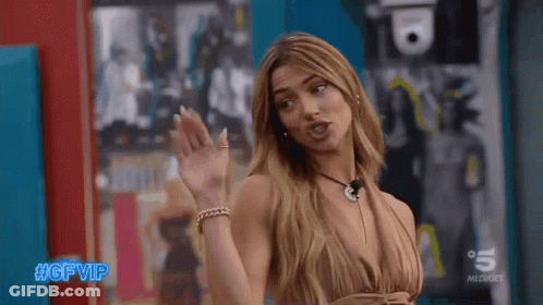 Woman In Revealing Dress Standing In Front Of Blue Wall Waving GIF