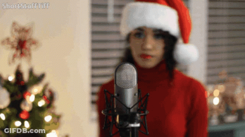 Woman In Santa Hat Standing In Front Of Microphone GIF