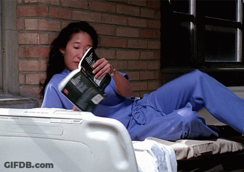 Woman In Scrubs Lying On Bed Reading Magazine GIF