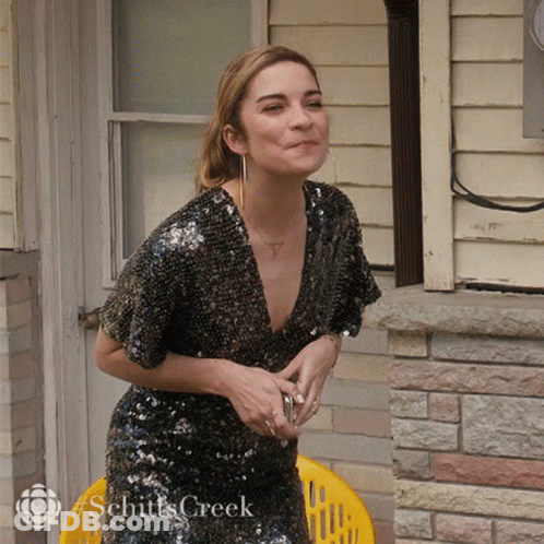 Woman In Sequined Dress Sitting In Front Of Brick Building Schitts Creek GIF