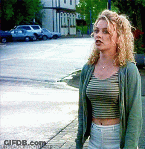 Woman In Striped Crop Top And Green Jacket On Sidewalk GIF