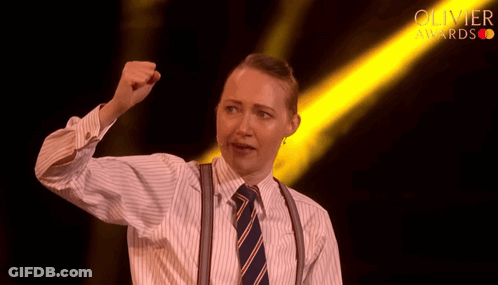 Woman In Striped Shirt And Suspenders Holding Fist Up Before Olivier Awards Light GIF