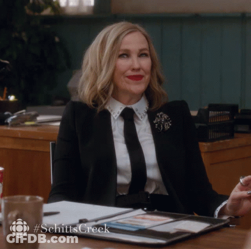 Woman In Suit And Tie At Desk With Hashtag Schitts Creek GIF