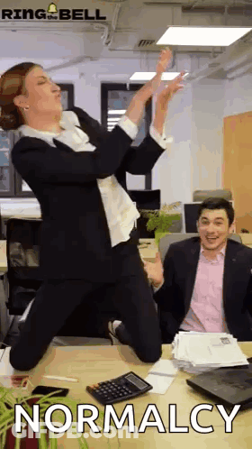 Woman In Suit Jumping In Front Of Man At Desk GIF
