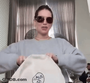 Woman In Sunglasses And Blue Sweater Holding White Bag GIF