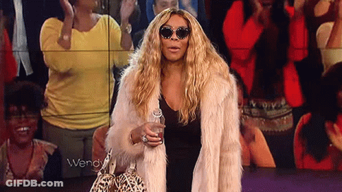 Woman In Sunglasses And Fur Coat Holding Drink In Crowd GIF