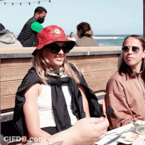Woman In Sunglasses And Red Hat With Letter A Sits At Table Outside GIF