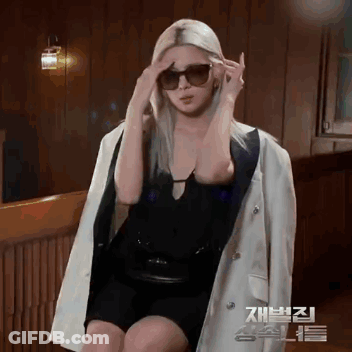 Woman In Sunglasses And White Jacket Sitting In Front Of Wooden Wall GIF