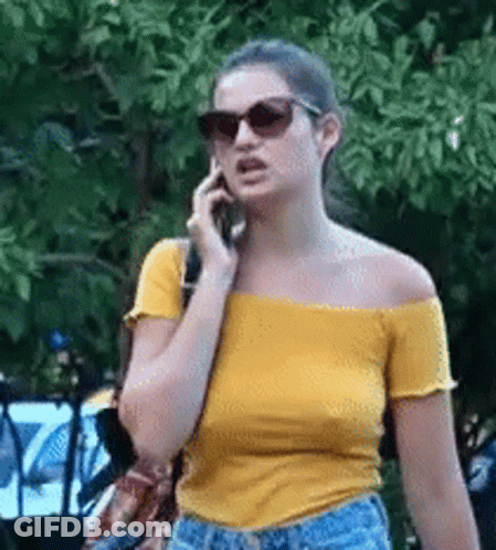 Woman In Sunglasses And Yellow Off-Shoulder Top Talking On Phone GIF